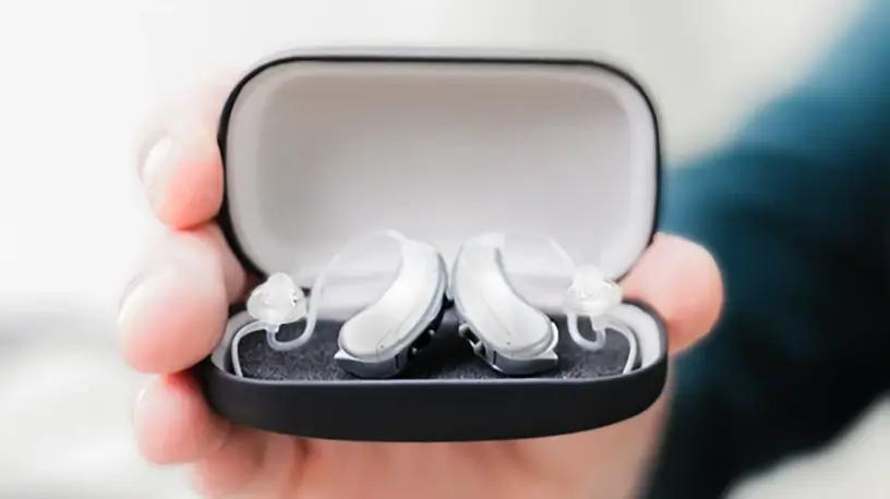 Hands holding the Lexie Lumen Self-fitting OTC hearing aids and case.