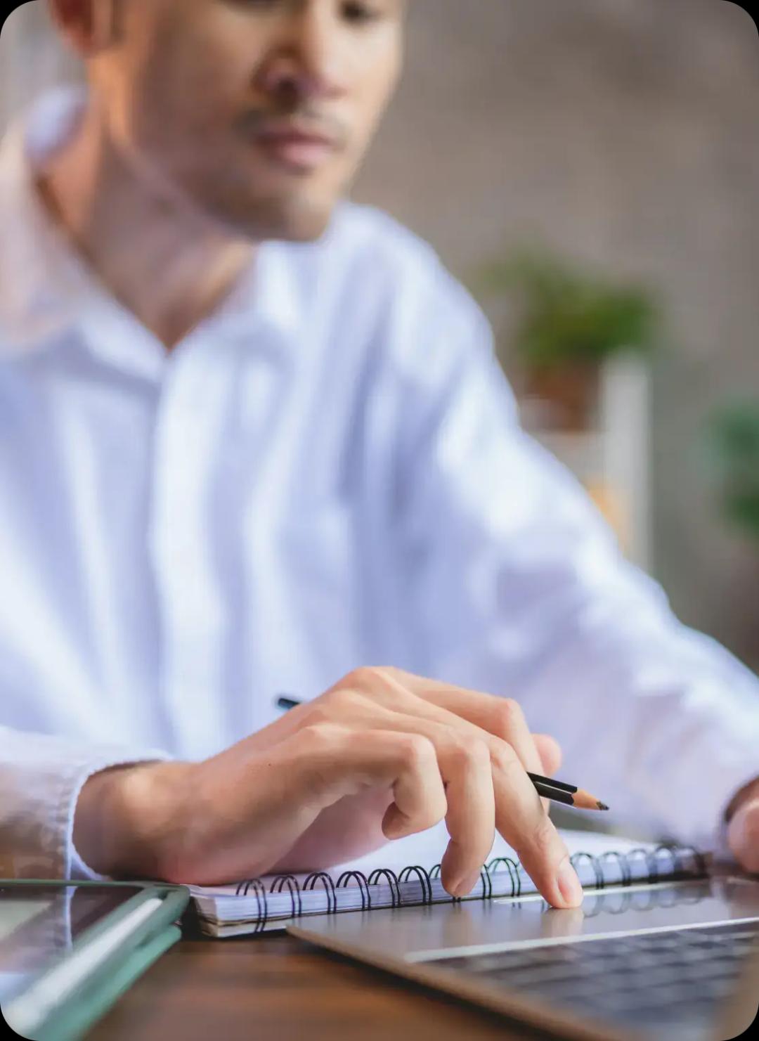 A man taking notes and working on a laptop