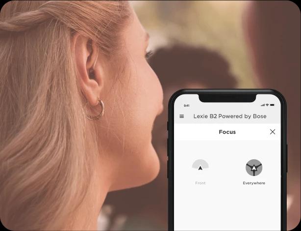 A group of woman eating at a restaurant, one adjusting her Lexie hearing aids on the Lexie app.