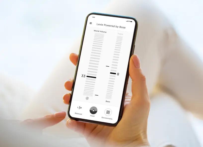 Hand holding a phone adjusting settings for the Lexie B1 hearing aids on the Lexie app.