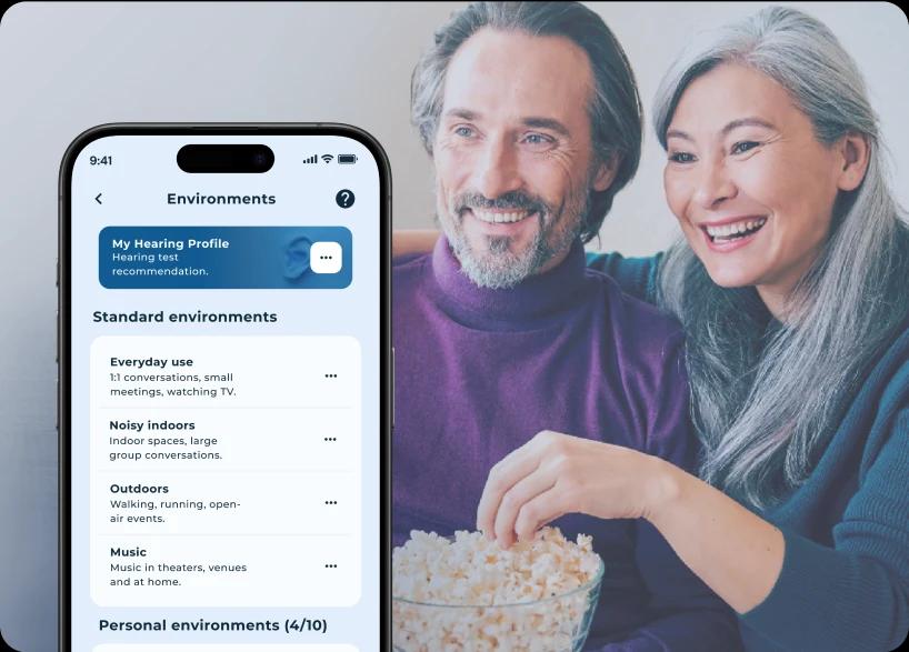 Man and woman watching TV and eating popcorn and the Lexie app showcasing listening environments.