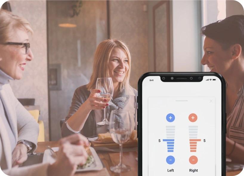 A group of woman eating at a restaurant, one adjusting her Lexie Lumen hearing aid settings on the Lexie app.