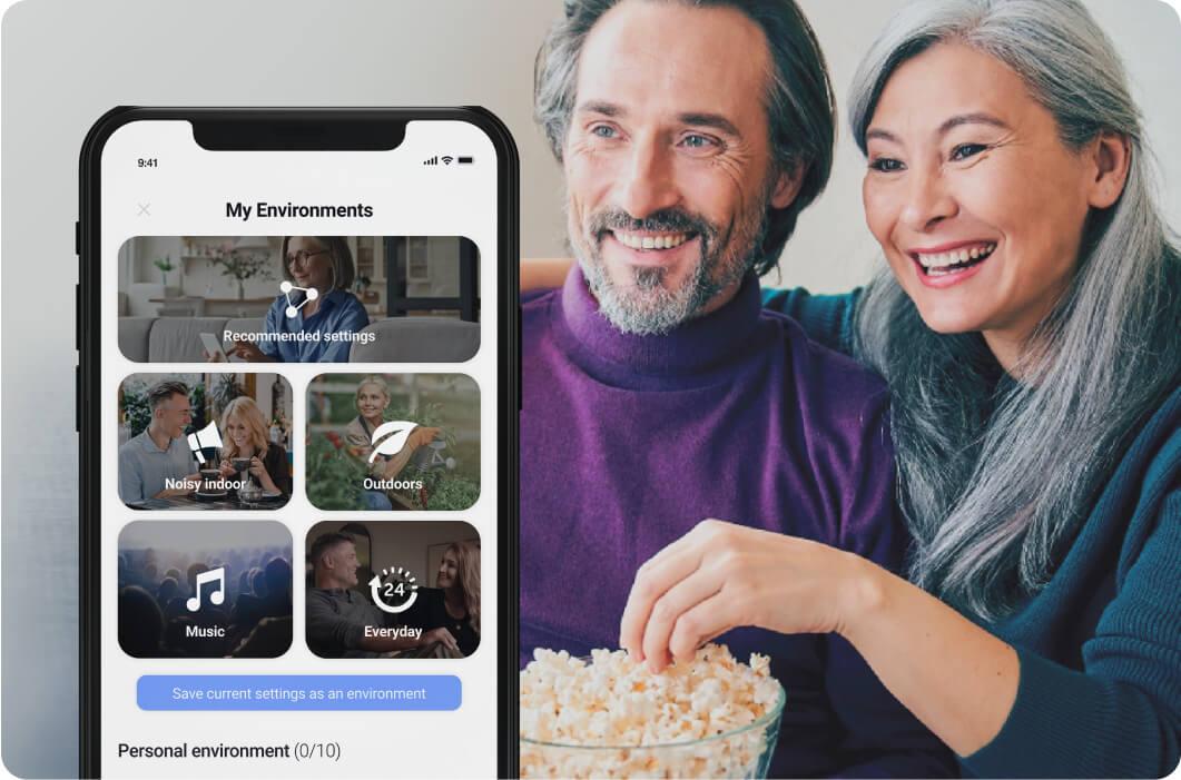 Man and woman eating popcorn and watching TV with Lexie hearing aids.