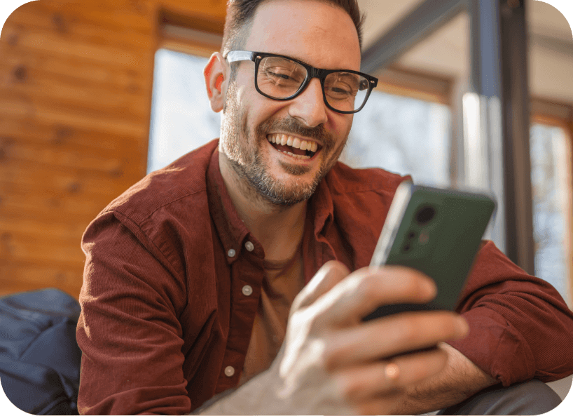 Man wearing glasses holding and smiling at his phone.