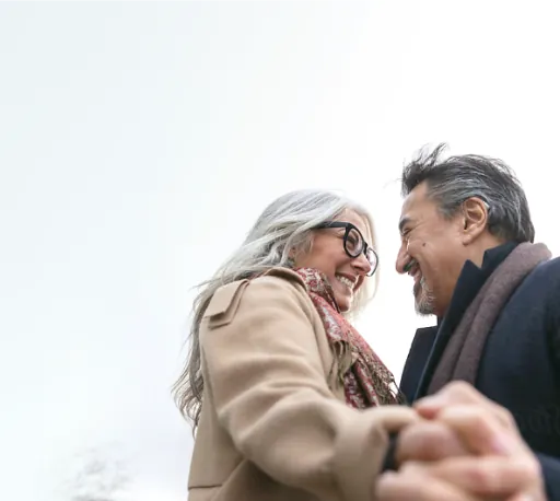 Man and woman in winter wear holding hands and smiling at each other. The man is wearing Lexie B2 hearing aids.