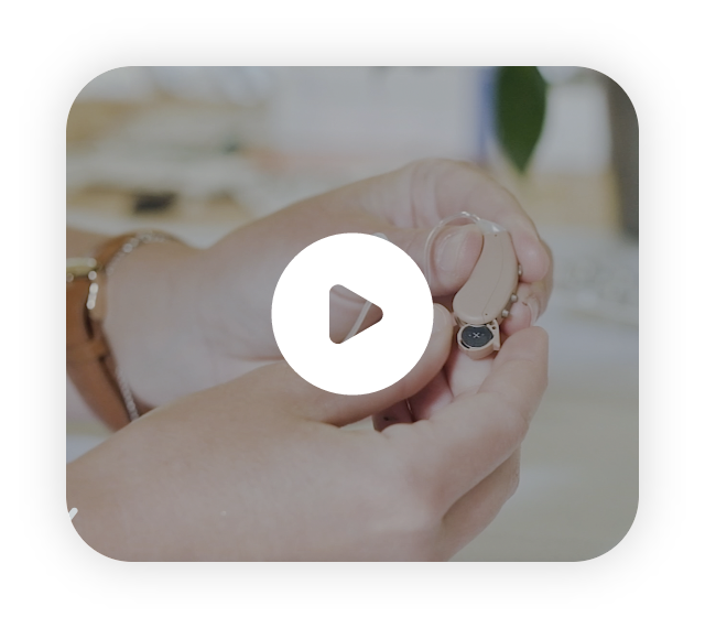 A hand holding a Lexie Hearing Aid product. Click to play the video.