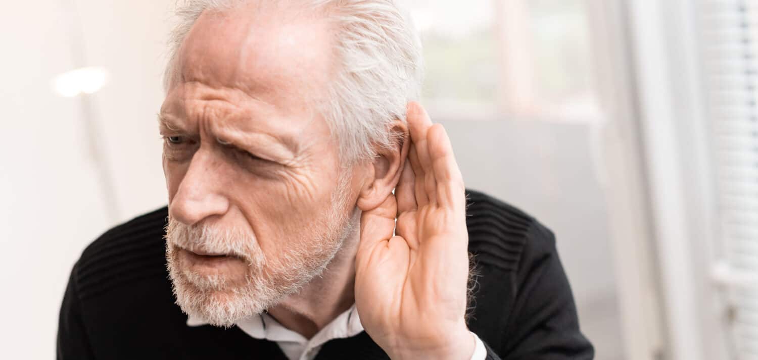 Elderly man cupping his ear to hear better, a common sign of hearing loss