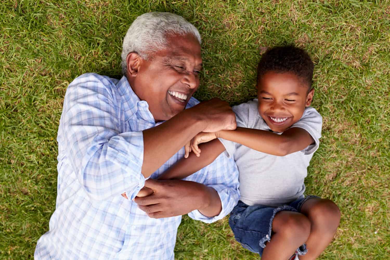 Grandfather and grandson laughing and lying in the grass