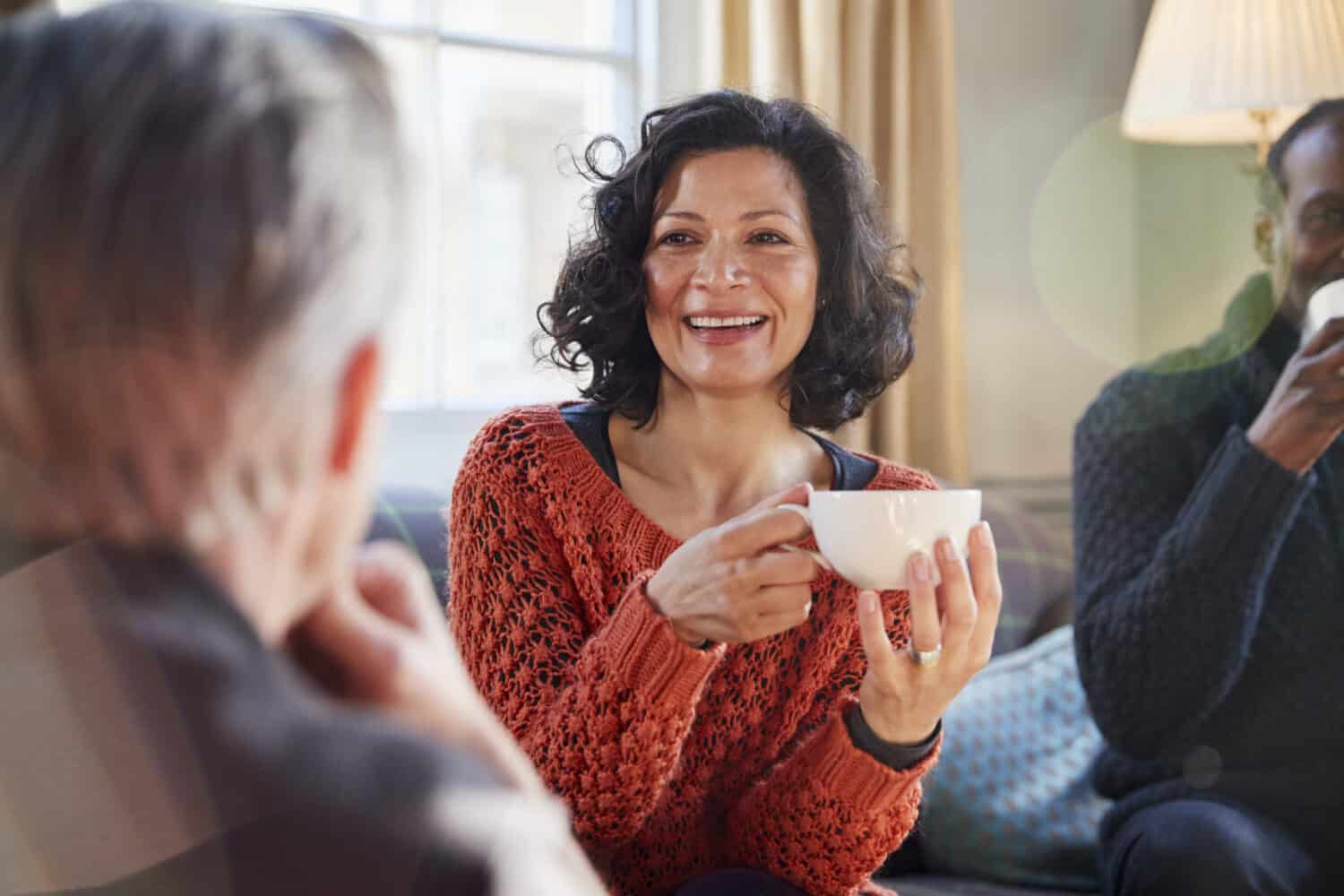 Middle aged woman meeting friends around table, wearing her best online hearing aid.