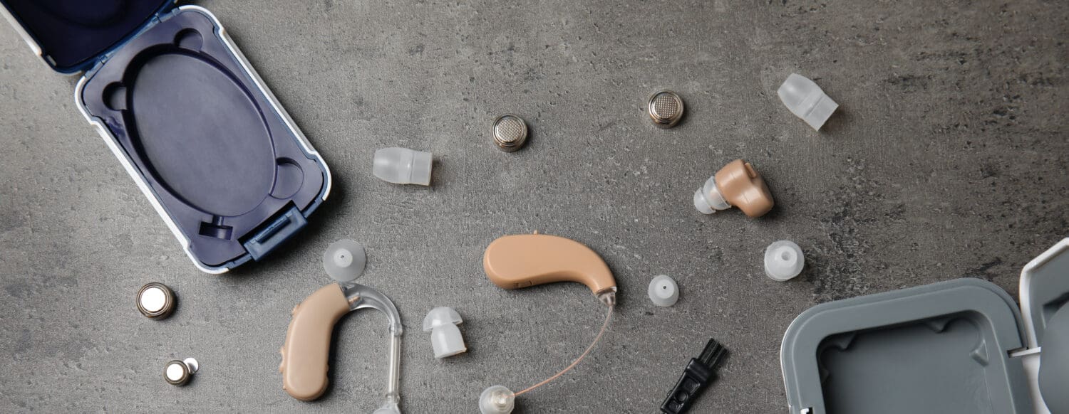 Flat lay composition with hearing aids and accessories on grey background, showcasing a quality hearing aid.