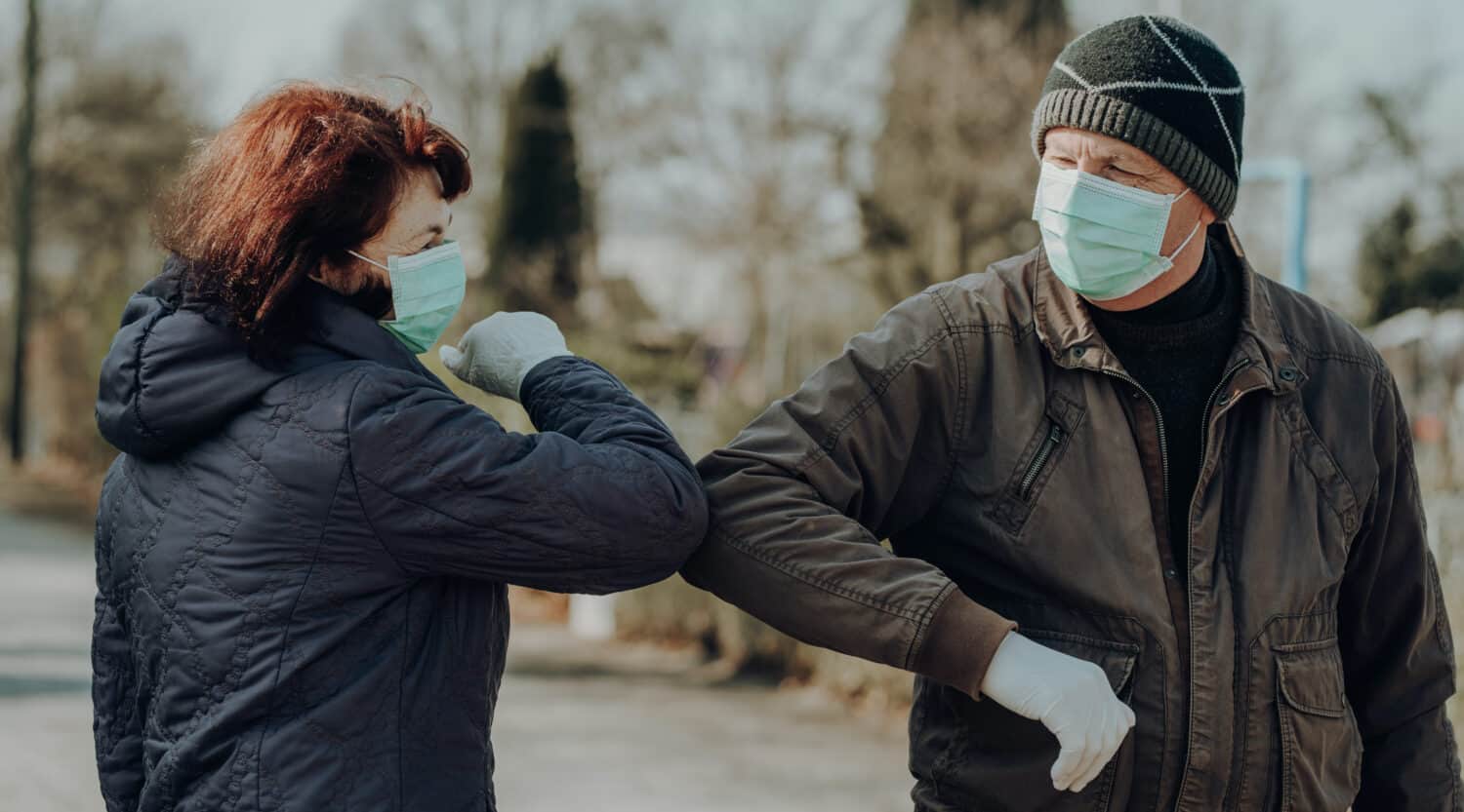 Two people wear face masks and premium hearing aids during the COVID-19 pandemic.