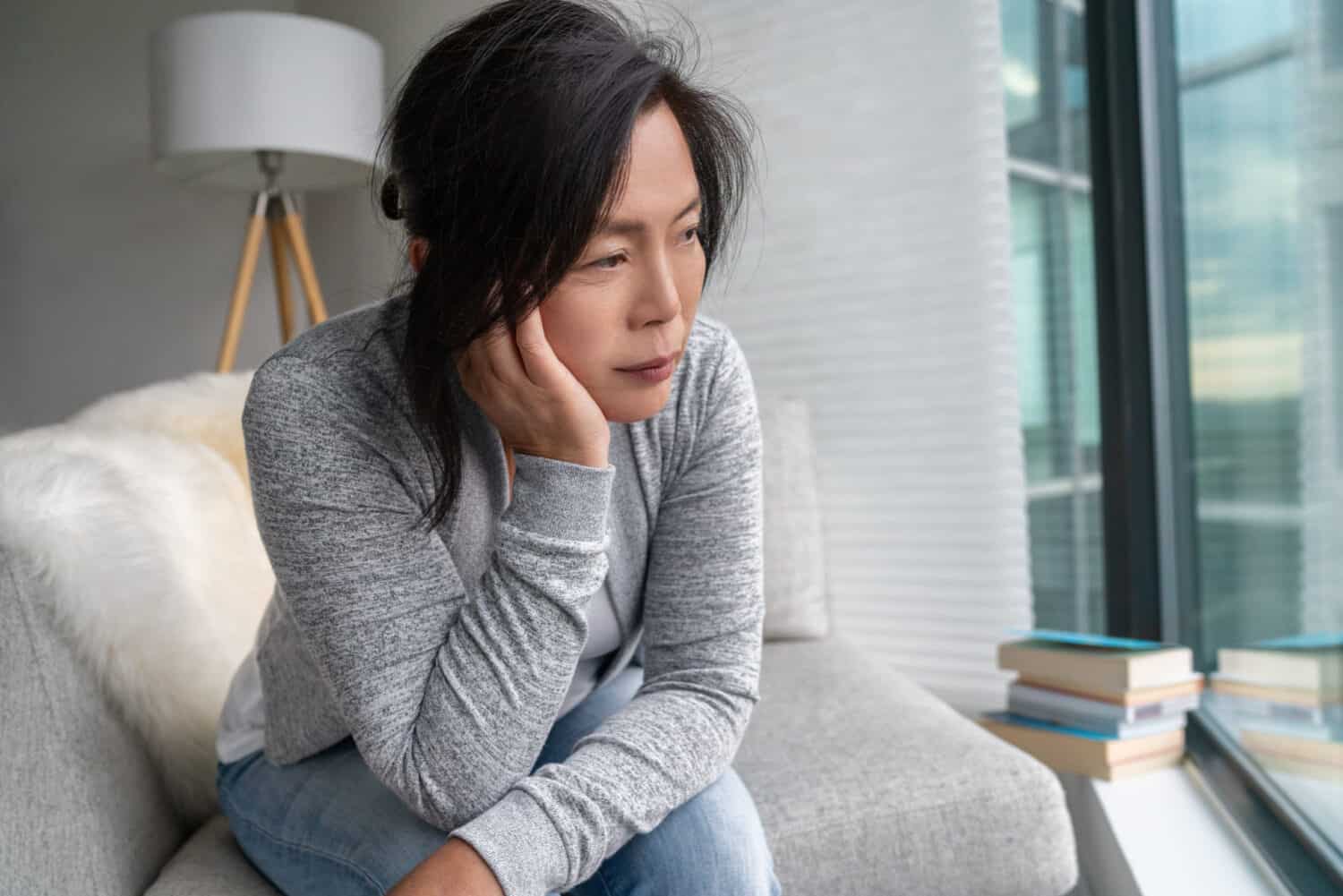 Woman wearing a hearing aid sits on the couch looking frustrated and about to call a hearing aid specialist for assistence with her premium hearing aid
