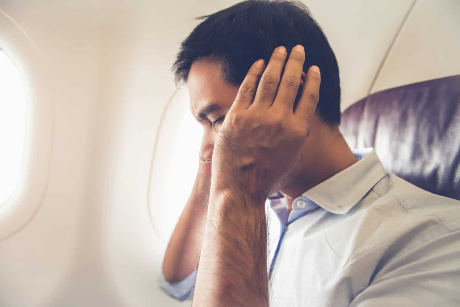 Man sitting on an airplane with his hands over his ears