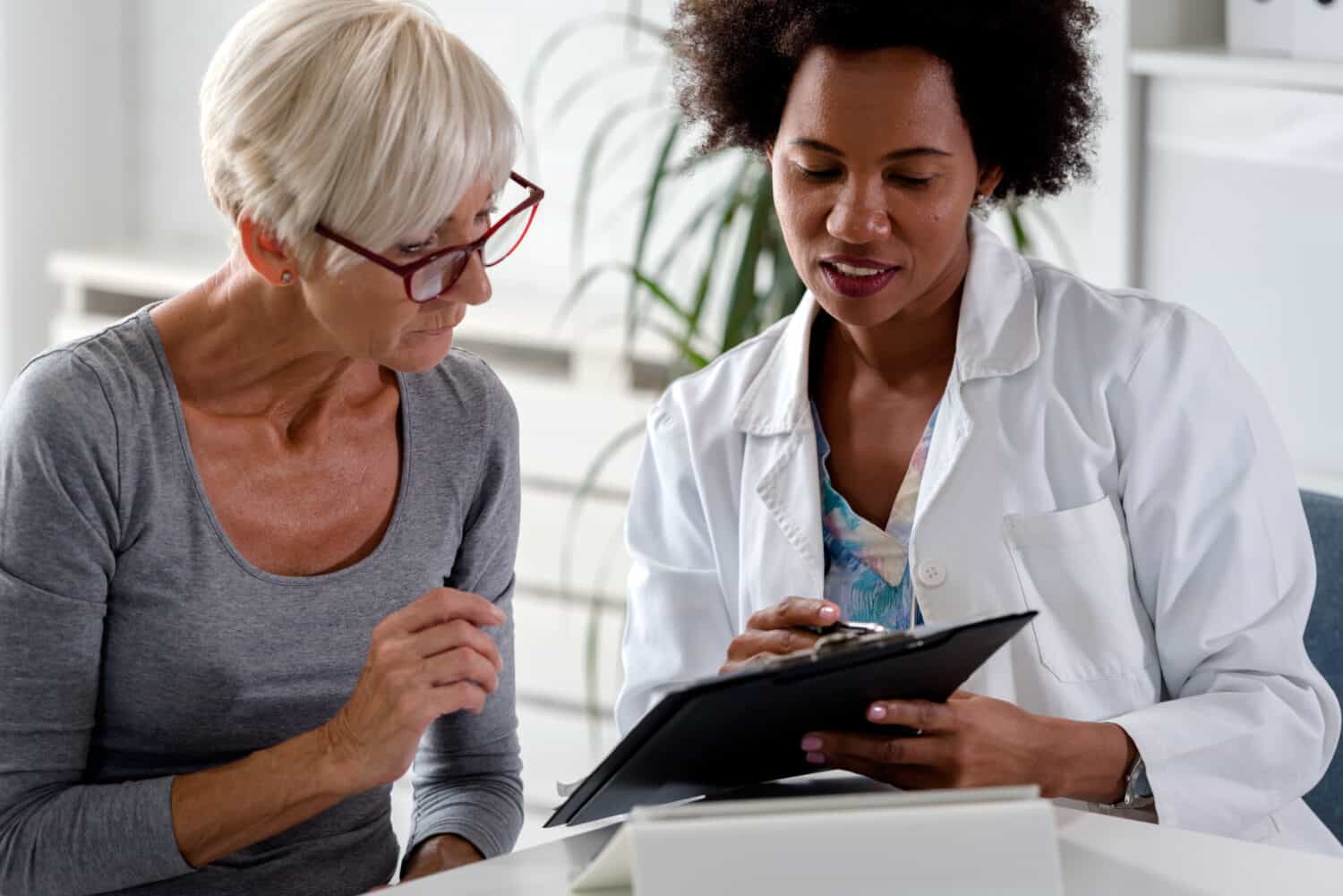Woman consulting a female hearing healthcare expert about her self-diagnosed hearing loss at a table holding a tablet.