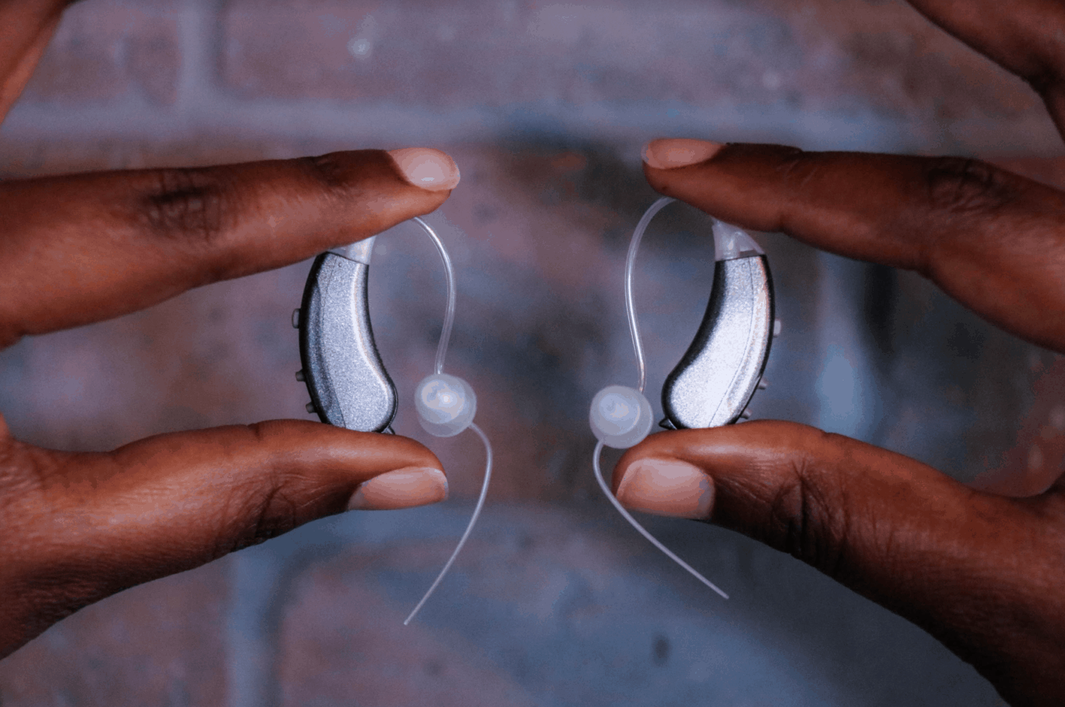 Two silver, behind-the-ear hearing aids in the hands of a hearing aid expert