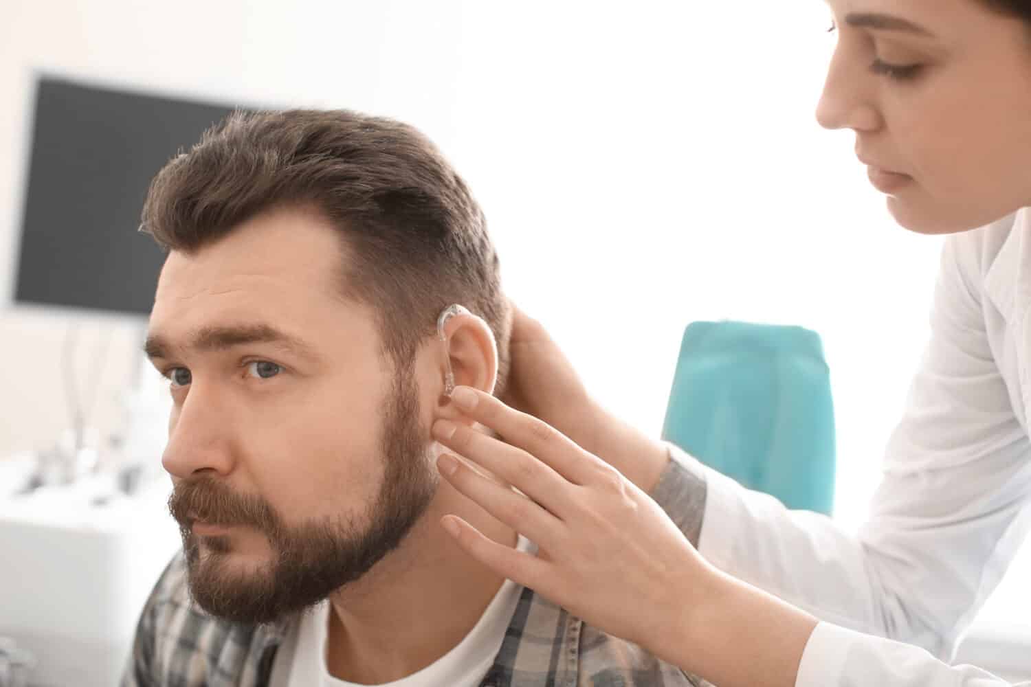Man being fitted with a hearing aid by a woman hearing aid expert.