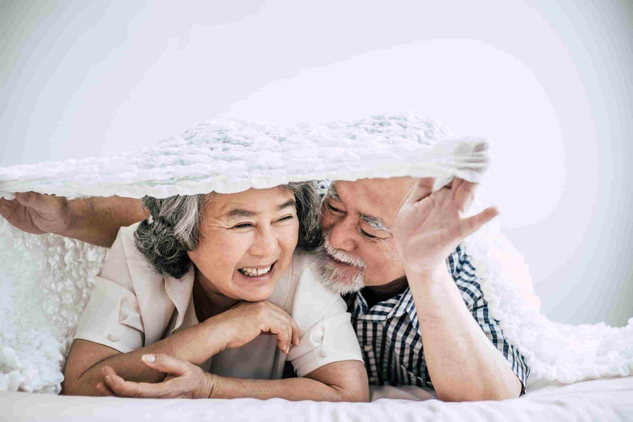 Man and woman laying in bed laughing and discussing rechargeable hearing aids
