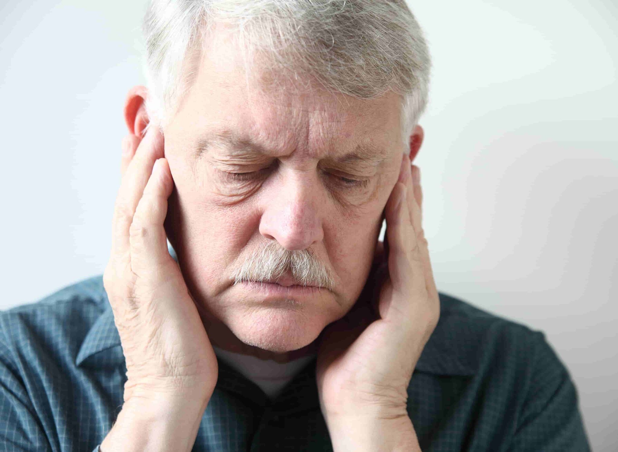 Senior man holding his ears due to experiencing hearing aid feedback