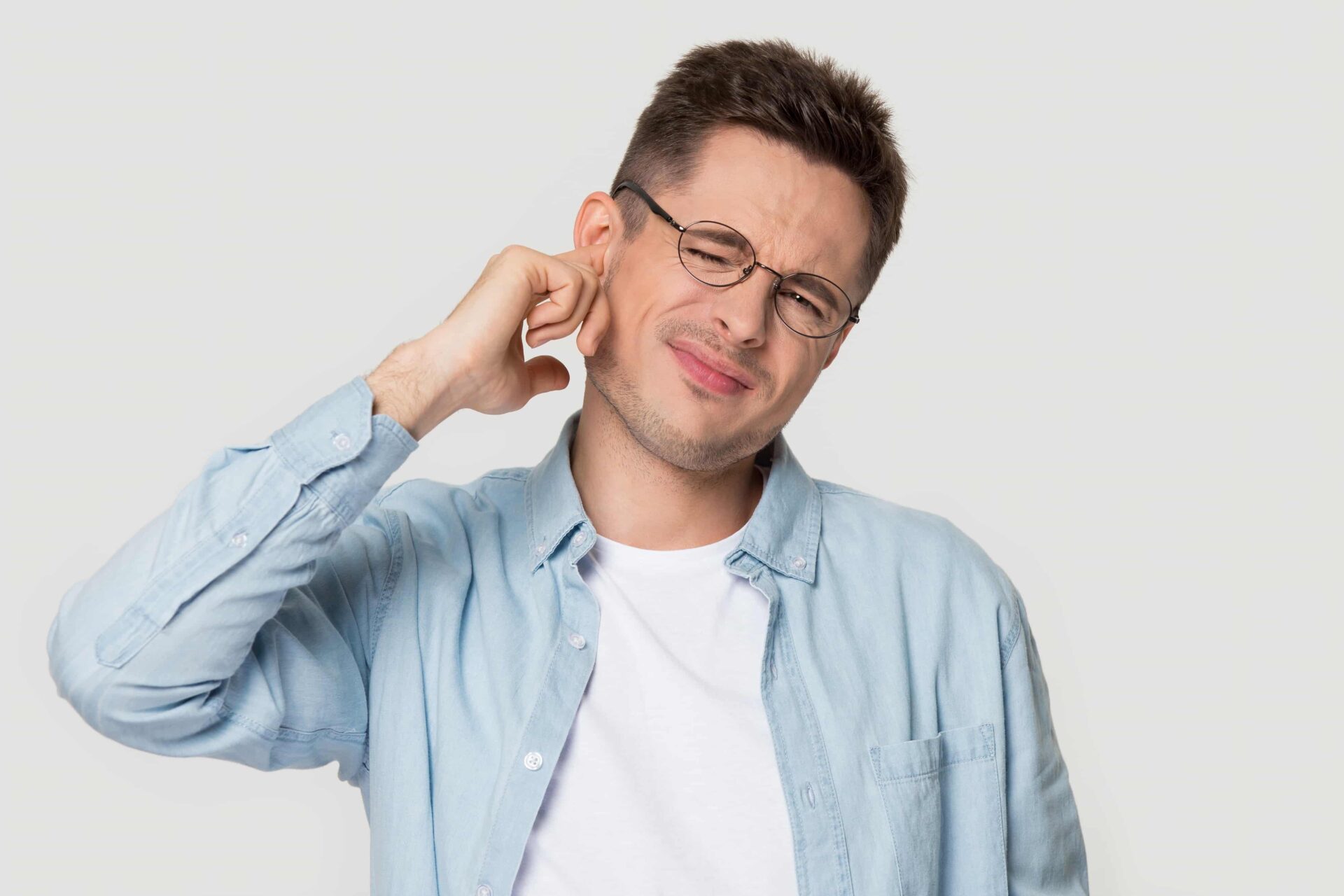 Young man wearing glasses holding his ear out of pain or a crackling in his ear.