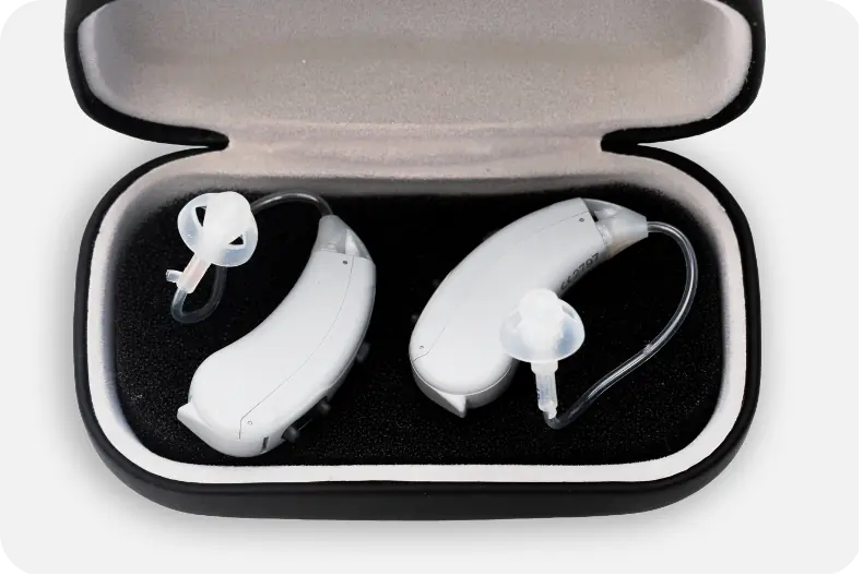Light gray Lexie Lumen hearing aids in a black and gray Lexie hearing aid carry case.