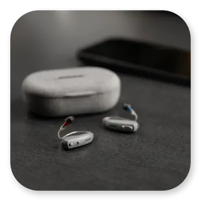 Lexie B1 Lifestyle | Hearing aids lying on a table with carry case behind thumbnail