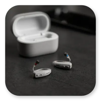 Lexie B2 Lifestyle | Hearing aids lying on a table with carry case behind thumbnail