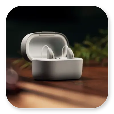 Lexie B2 Lifestyle | Open hearing aid case with hearing aids inside on a desk next to plants thumbnail